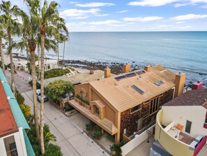 A coastal building with a flat roof, solar panels, and a balcony overlooking the beach.