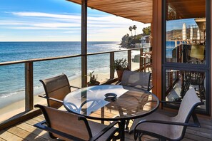 A deck with a glass table and chairs overlooking a beach.