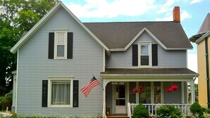 A two-story house with a porch, a small garden, and an American flag.