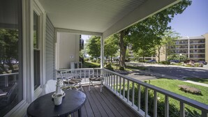 A covered porch with a table and chairs, overlooking a street with parked cars and a building with balconies.