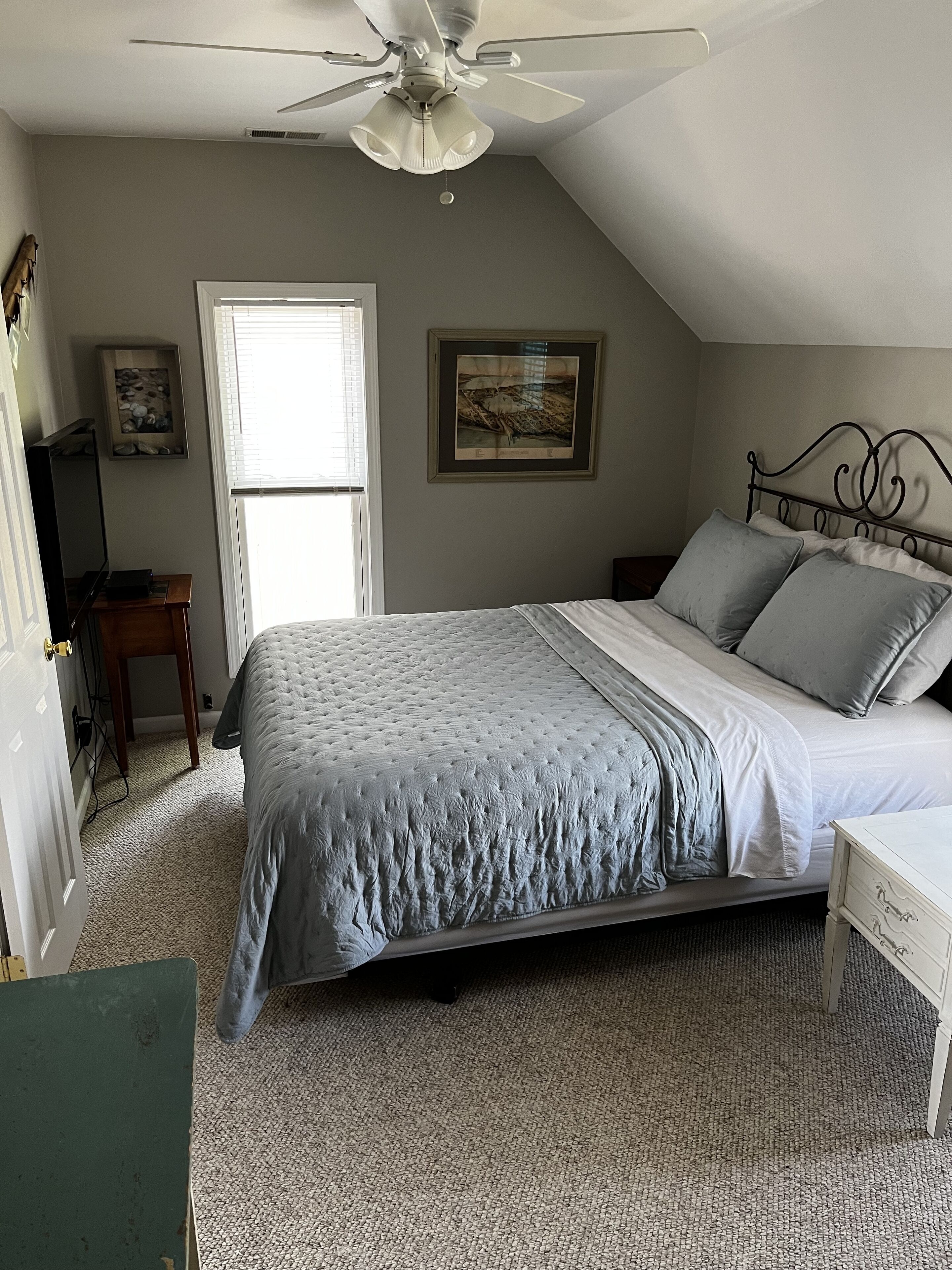 A bedroom with a bed, a ceiling fan, a window, and a framed picture on the wall.