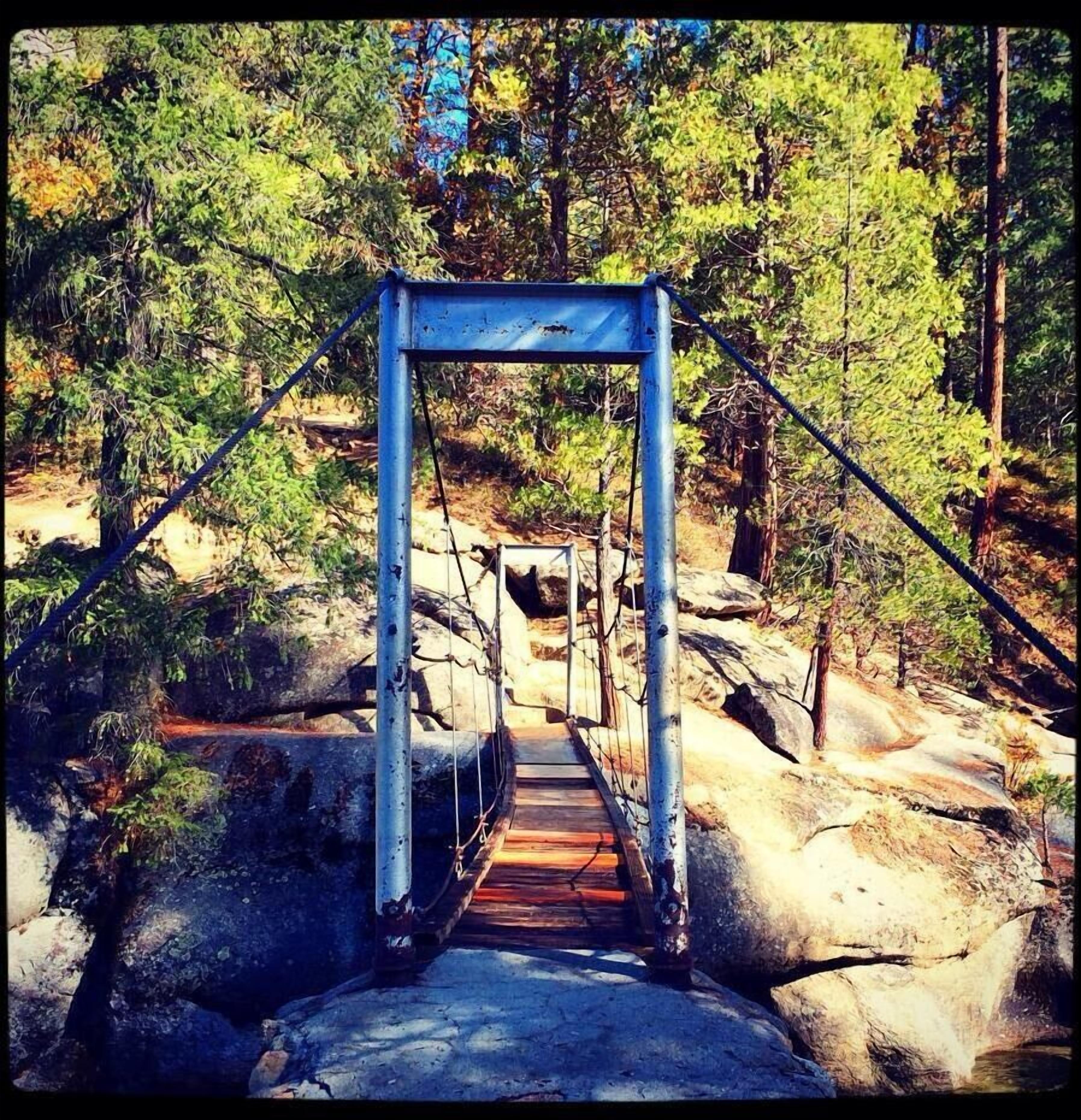 Une structure de pont métallique située dans une zone boisée, avec une passerelle en bois.