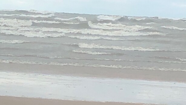 Ein Strand mit brechenden Wellen am Ufer unter einem bewölkten Himmel.