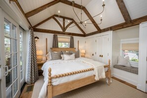 A bedroom with a wooden bed, a window with curtains, a chandelier, and a bench by the window.