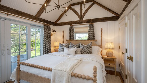 Un dormitorio con cama de madera, un ventanal grande y una araña.