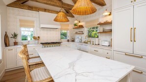 Una cocina amplia con una isla grande, armarios blancos y vigas de madera en el techo.