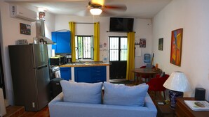 Eine kompakte Küche mit Kühlschrank, Herd und blauen Schränken. Es gibt einen Essbereich mit Tisch und Stühlen sowie ein Sofa im Wohnbereich.