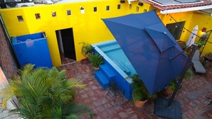Ein Innenhof mit einem blauen Pool, Blumentöpfen und einer gelben Wand.
