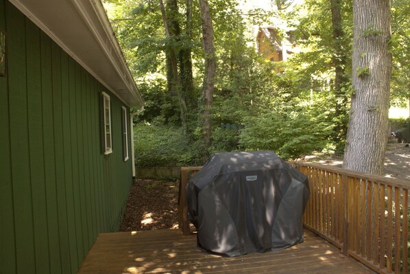 A green building with a covered grill and a wooden deck.