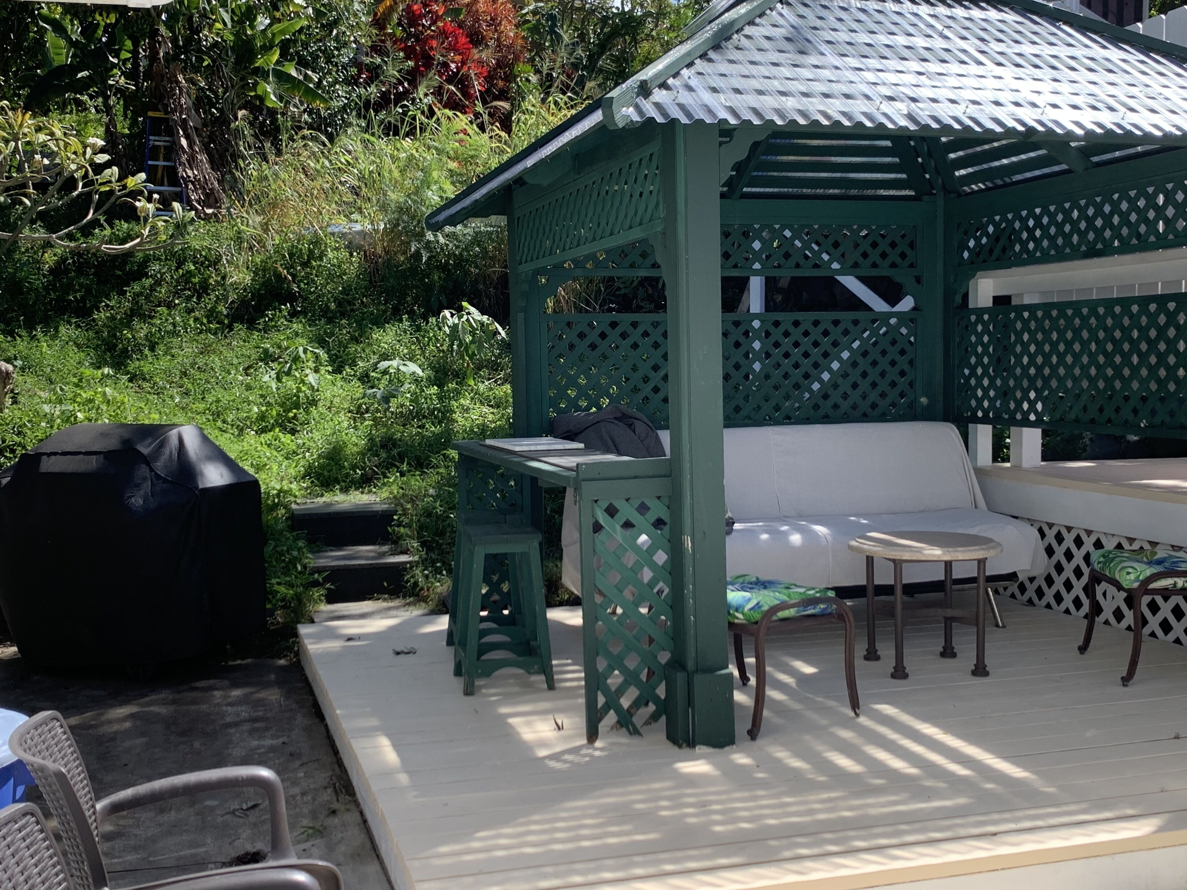 Een overdekt terras met een tafel en stoelen, omgeven door groen.