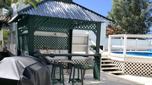 Un espace extérieur aménagé avec des sièges, protégé du soleil, et une piscine en arrière-plan.