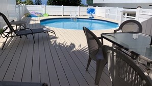 Un espace piscine doté d’une terrasse en bois, de chaises en métal et d’une table en verre.