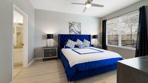 A bedroom with a bed, nightstands, a ceiling fan, a window with blinds, and a door leading to a bathroom. - Paradise Villa, No rear neighbors, Minutes from Disney (Kissimmee)