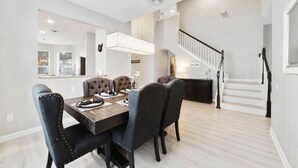 A dining area with a dark wood table and tufted chairs, a staircase, and a "WELCOME" sign. - Paradise Villa, No rear neighbors, Minutes from Disney (Kissimmee)