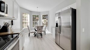 A modern kitchen with white cabinetry, a stainless steel refrigerator, and a dining area with patterned chairs. - Paradise Villa, No rear neighbors, Minutes from Disney (Kissimmee)