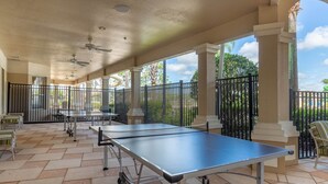 An outdoor covered area with a ping pong table, chairs, and a patio with a view of the surrounding landscape.