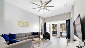 A modern living room with a grey sofa, a round coffee table, and a ceiling fan. - Paradise Villa, No rear neighbors, Minutes from Disney (Kissimmee)