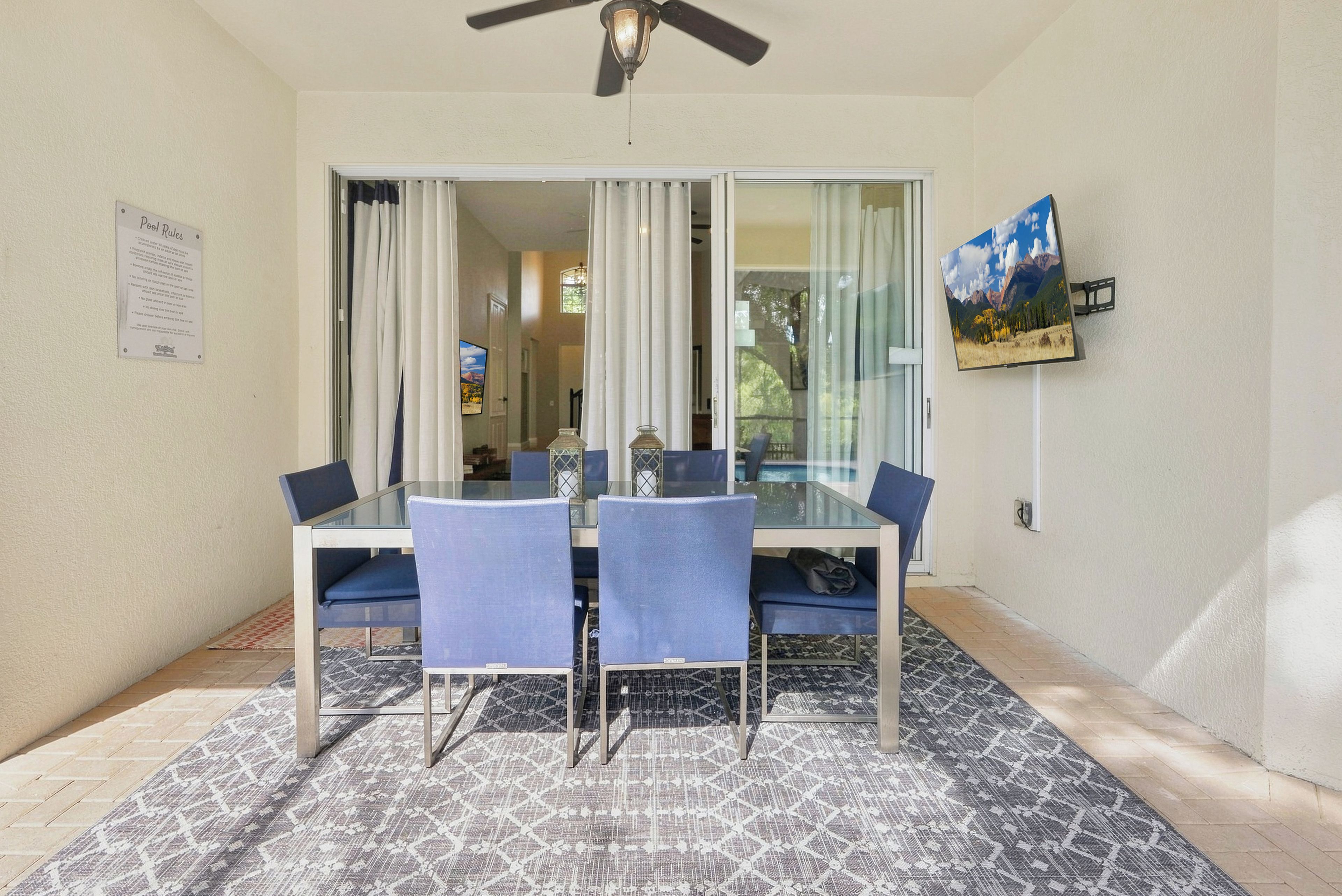 A dining area with a glass table and chairs, a ceiling fan, and a view of the interior through a glass door.