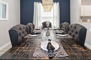 A dining room with a dark wooden table, grey upholstered chairs, and a chandelier.
