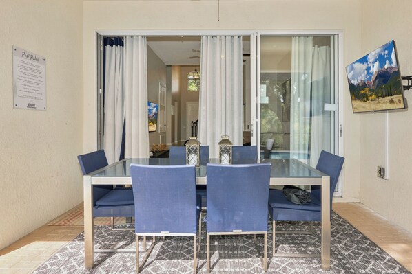 A glass-top dining table with blue chairs, a chandelier, and a painting on the wall. - Paradise Villa, No rear neighbors, Minutes from Disney (Kissimmee)