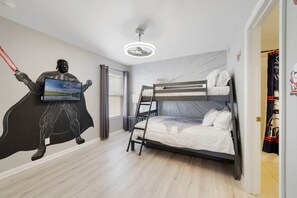 Une chambre avec un lit superposé, un ventilateur de plafond, un téléviseur fixé au mur et une fresque représentant Dark Vador.