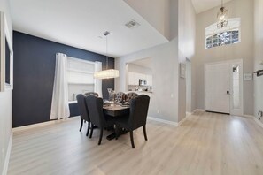 A dining area with a dark wood table and chairs, a chandelier, and a view of a kitchen in the background. - Paradise Villa, No rear neighbors, Minutes from Disney (Kissimmee)