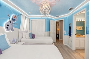 A bedroom with two beds, a chandelier, and a bathroom with a mirror and sink.