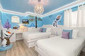 Une chambre à coucher avec deux lits, une table de chevet, une commode, un lustre et des décorations murales, notamment un château et un bonhomme de neige.