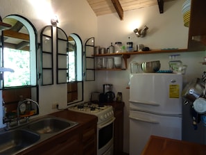 A compact kitchen with a gas stove, sink, and white refrigerator. There are shelves above the stove holding various kitchen items. - Pool, stunning ocean view, quiet, stairway to beach, ECO house (Montezuma)