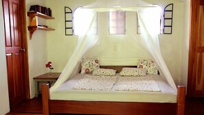 Una cama individual con dosel, una mesita de noche con un florero y un armario de madera.