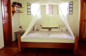 A single bed with a canopy, a bedside table with a vase of flowers, and a wooden wardrobe. - Pool, stunning ocean view, quiet, stairway to beach, ECO house (Montezuma)