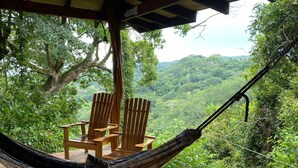 Un sillón hamaca colocado en una terraza con vistas a un exuberante paisaje boscoso.