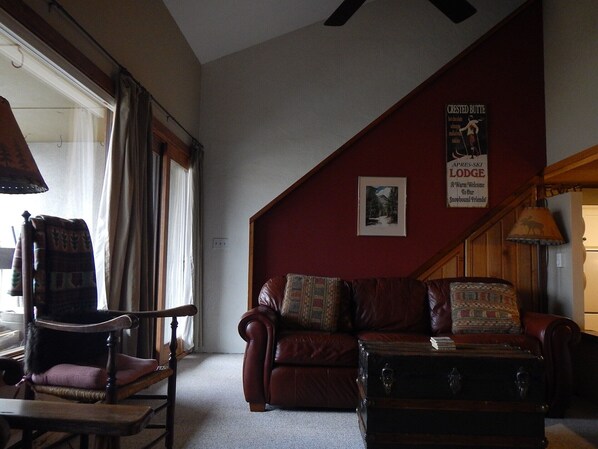 A cozy room with a leather sofa, a wooden chair, and a small table. There is a poster on the wall and a window with curtains. - Super location for Hiking,Biking, Aspen leaves are gorgeous!Come to check it out (Mt Crested Butte)