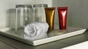 A bathroom shelf with a rolled towel, two glass bottles, and two toiletry tubes. - Ballena Dorada Hotel Boutique (Bahía Ballena)