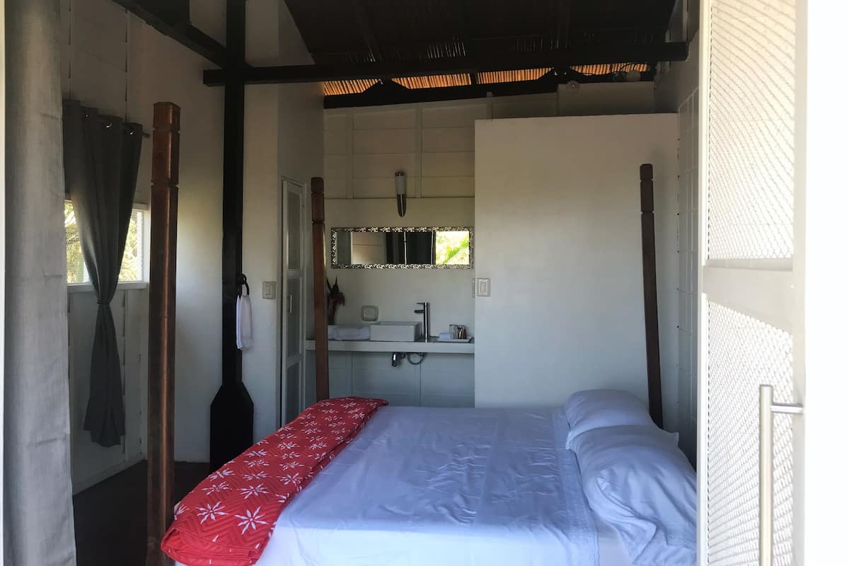 Ein Schlafzimmer mit Bett, Fenster mit Vorhängen, Spiegel, Waschbecken und Handtuchhalter.