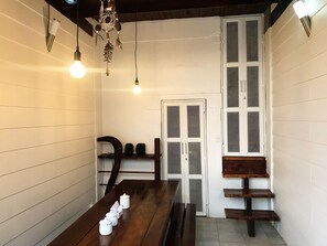 A room with a wooden table, white walls, a door with a mesh screen, and hanging light fixtures.