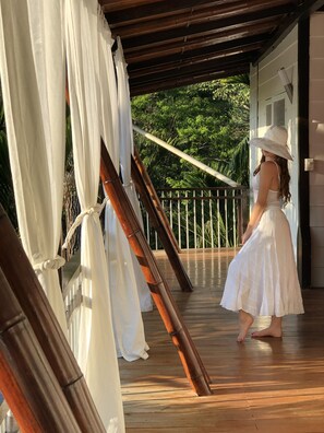 A woman in a white dress and hat standing on a wooden deck with white curtains and bamboo poles. - Ballena Dorada Hotel Boutique (Bahía Ballena)
