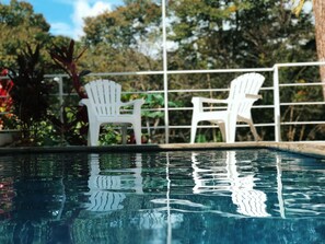 A swimming pool with clear water reflecting the surrounding trees and a white fence.