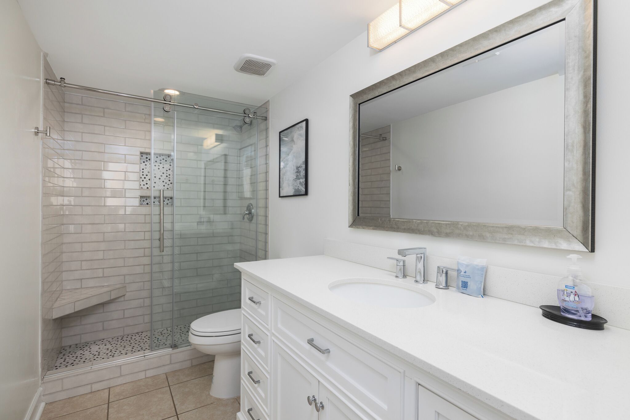 Un baño con cabina de ducha de vidrio, un lavabo blanco y un espejo grande.