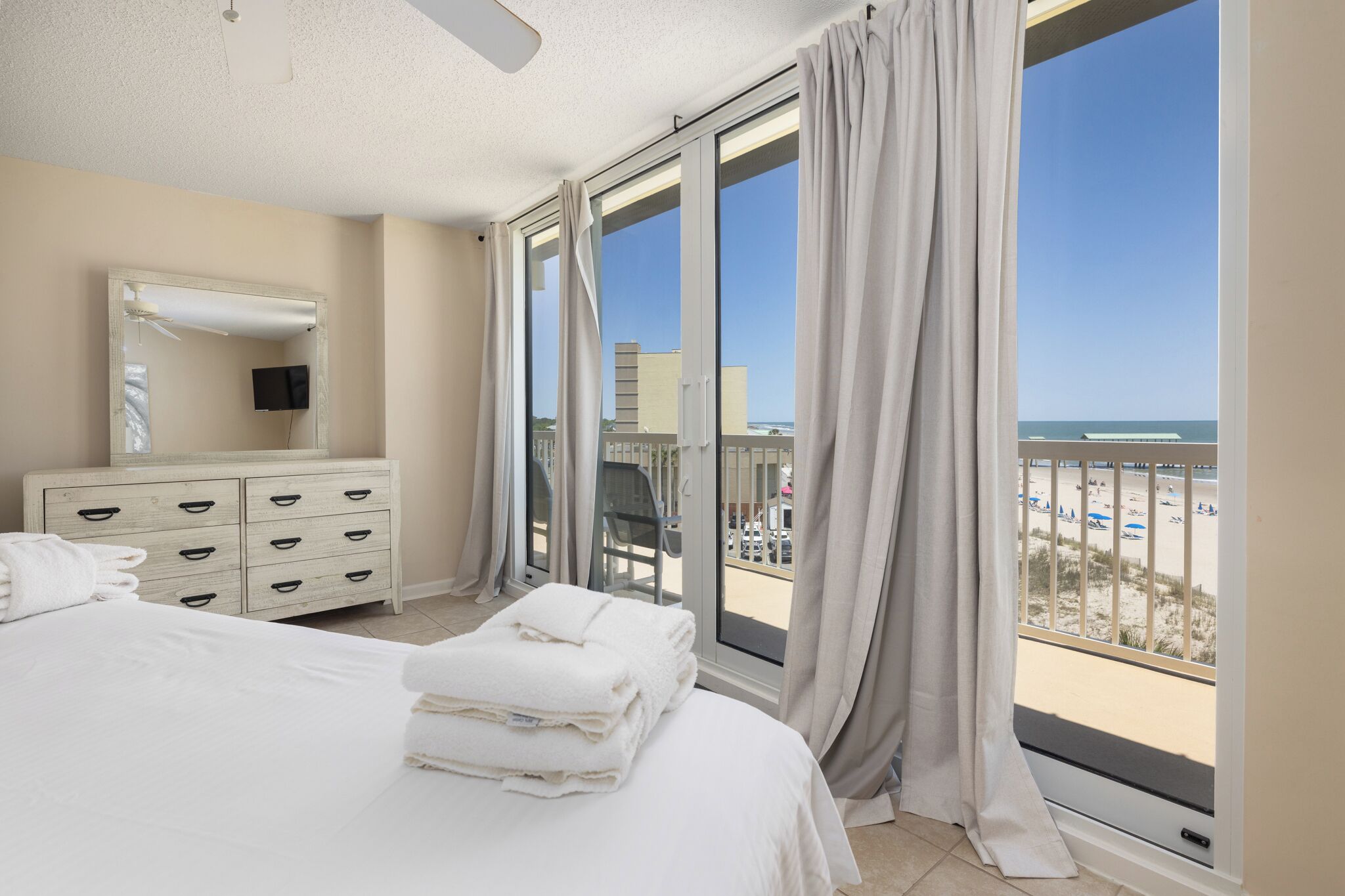 Habitación de hotel con cama, cómoda, espejo y balcón con vista a la playa.