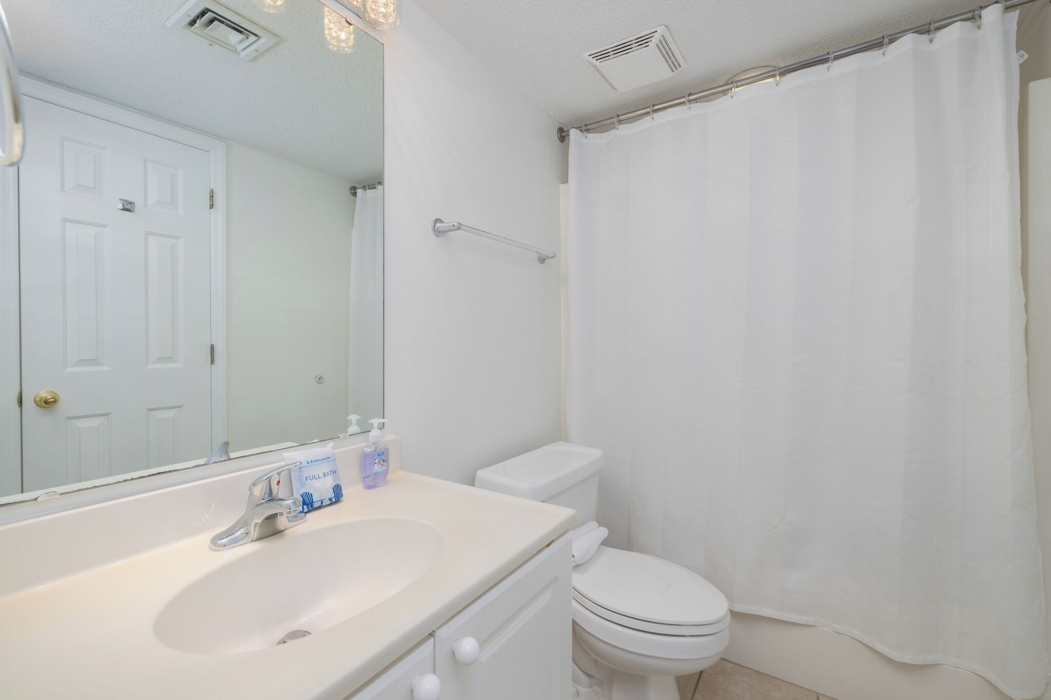 Une salle de bain avec un lavabo blanc, un miroir, des toilettes et un rideau de douche.