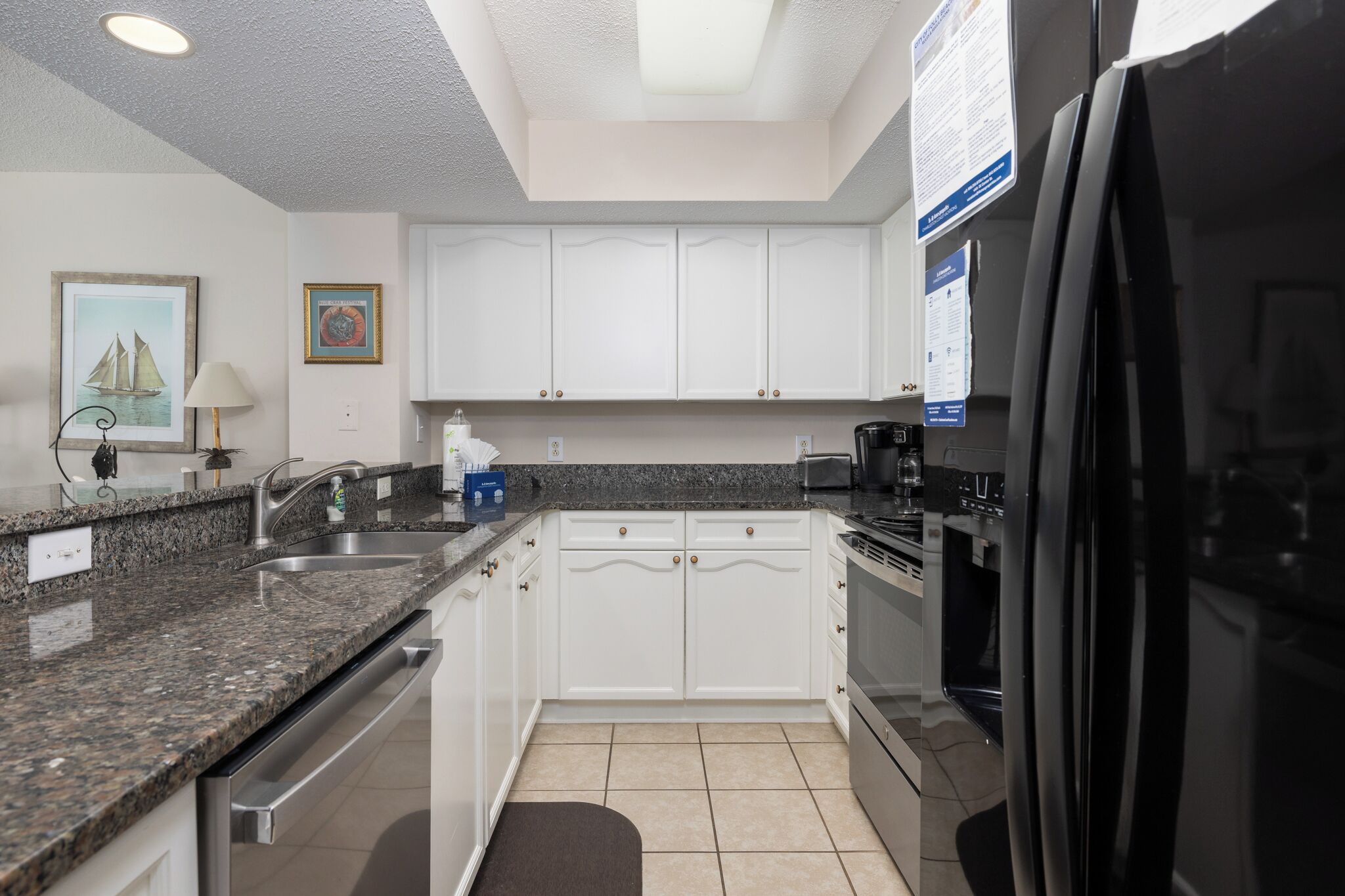 A modern kitchen with white cabinets, granite countertops, a stainless steel sink, and a black refrigerator.
