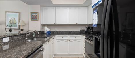 A modern kitchen with white cabinets, granite countertops, a stainless steel sink, and a black refrigerator.