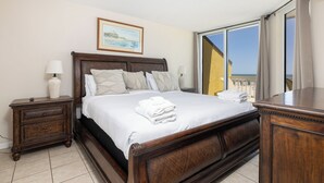 A bedroom with a large bed, a nightstand, a dresser, and a window with a view. - Stay @ The Good Life on Folly Beach (Folly Beach)