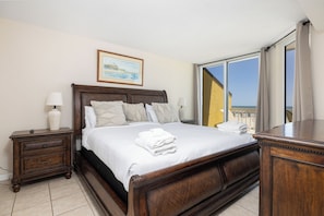A bedroom with a large bed, a nightstand, a dresser, and a window with a view. - Stay @ The Good Life on Folly Beach (Folly Beach)