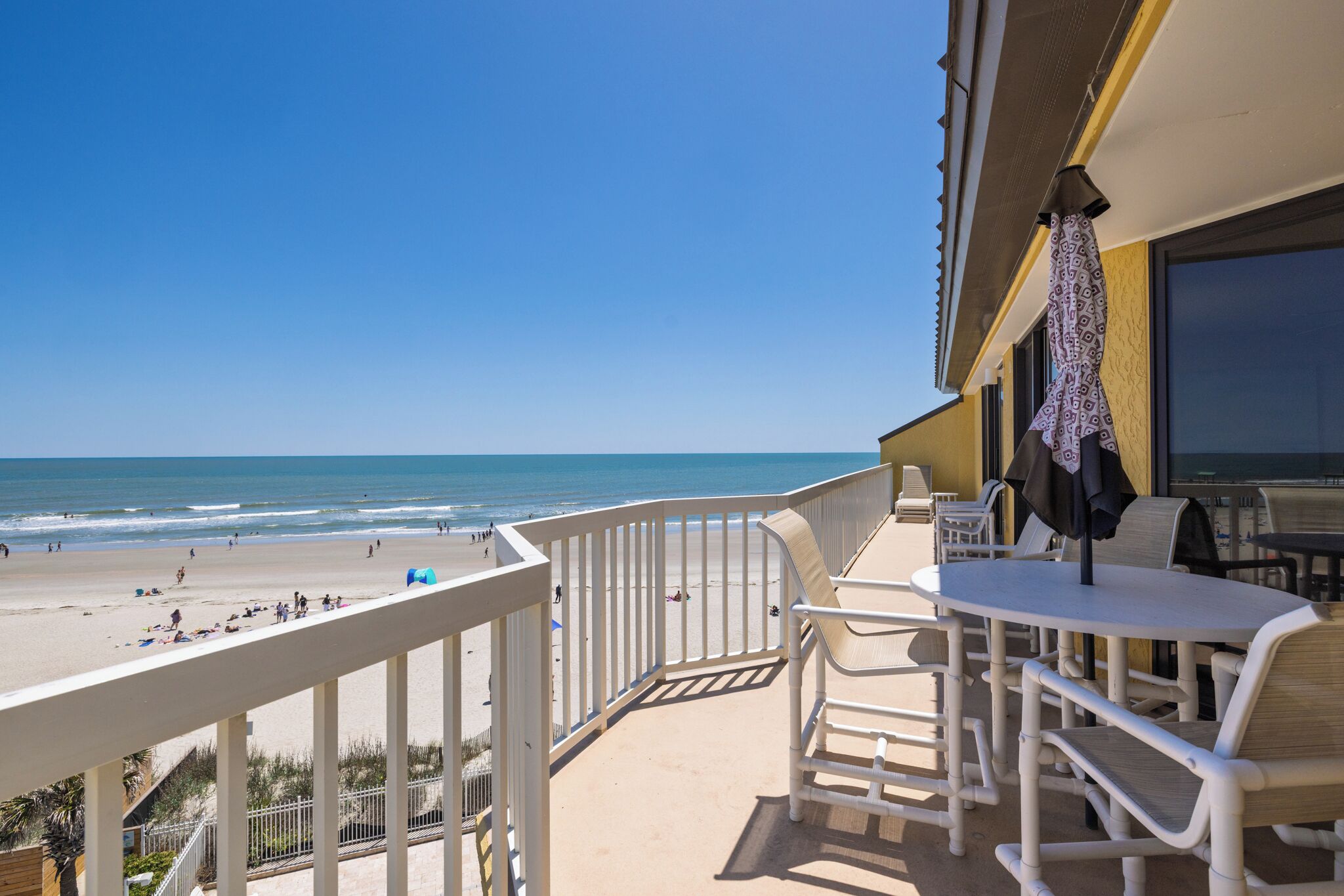 Un balcón con vista a la playa, mobiliario exterior y una zona cubierta con sombrillas.