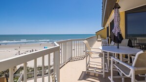 A balcony with a view of the beach, outdoor seating, and a covered area with umbrellas. - Stay @ The Good Life on Folly Beach (Folly Beach)