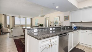 A modern kitchen with granite countertops, white cabinetry, and a dining area with a view. - Stay @ The Good Life on Folly Beach (Folly Beach)