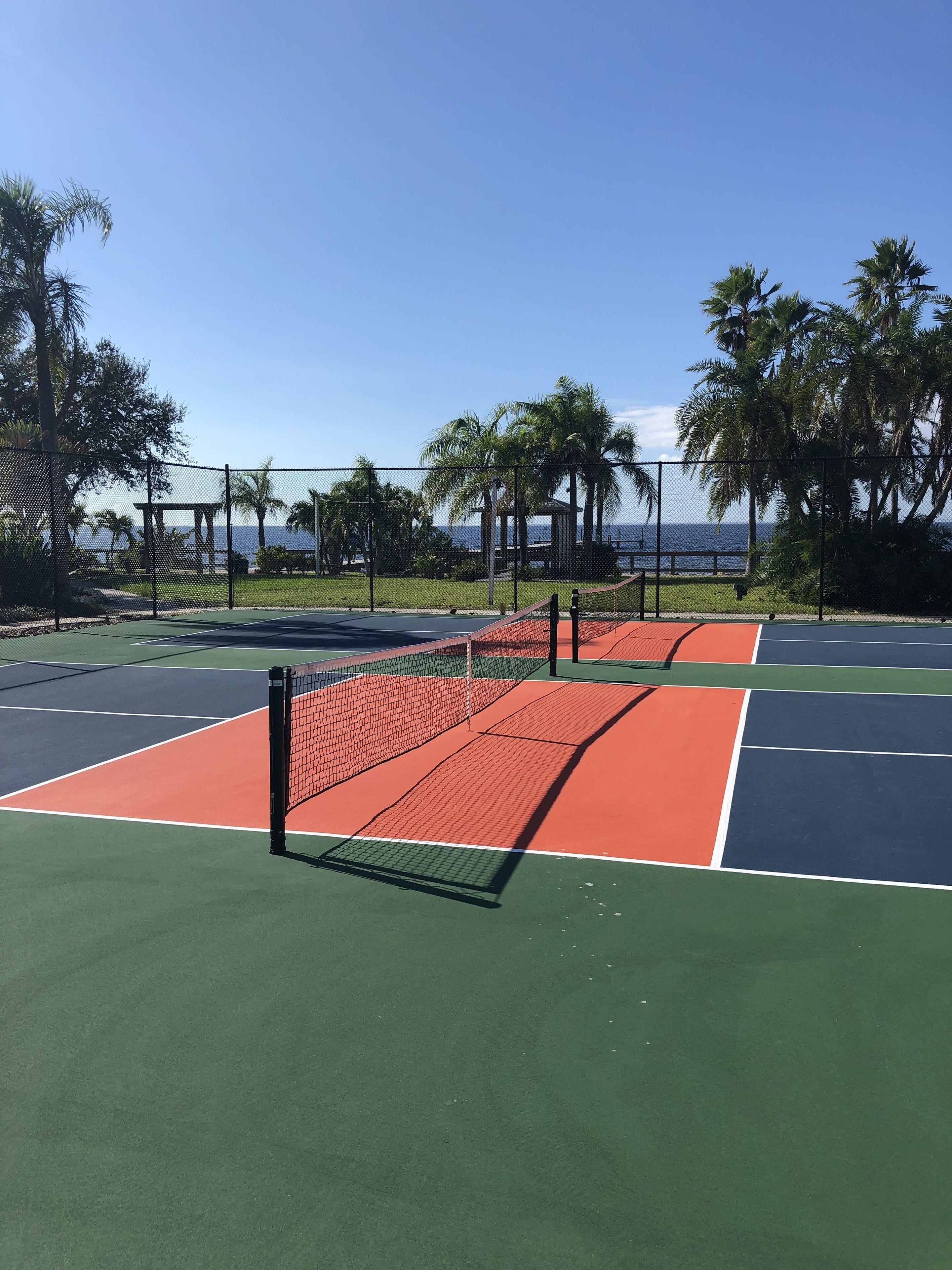 Ein Tennisplatz mit Netz, umgeben von Palmen und Blick aufs Meer.