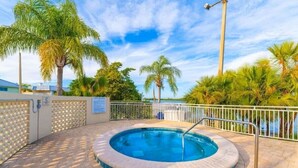 A circular hot tub surrounded by a brick patio, with palm trees and a view of the ocean in the background. - Beautiful New Luxury Townhome with Private Beach and Swimming Pools  (Ruskin)